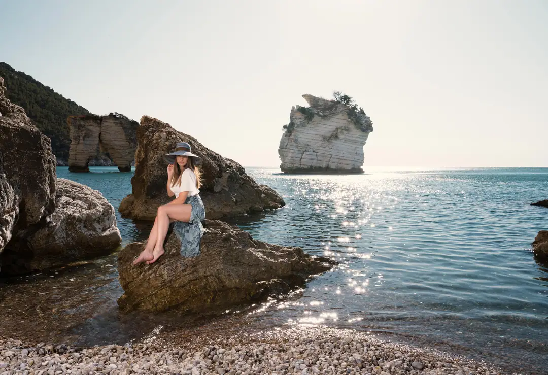 Woman in a wide-brim hat on the sea stacks of Baia delle Zagare